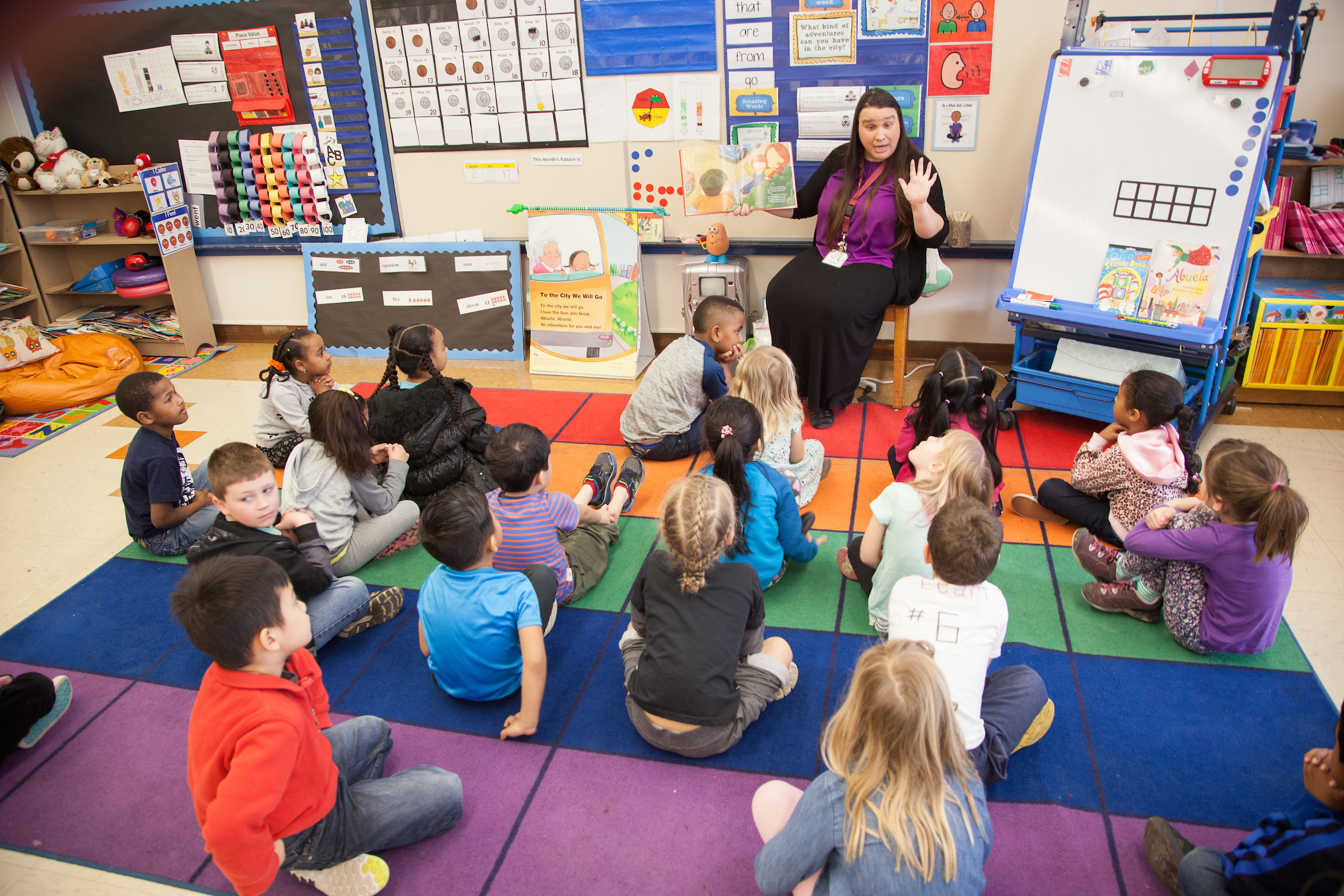 Elementary school teacher reading a book to kids seated on carpet